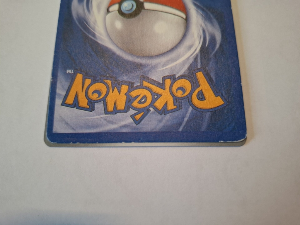 Nahaufnahme der unteren rechten Ecke einer Pokémon-Karte, die das Logo verkehrt herum auf einem blauen Hintergrund mit einer Pokéball-Grafik zeigt.